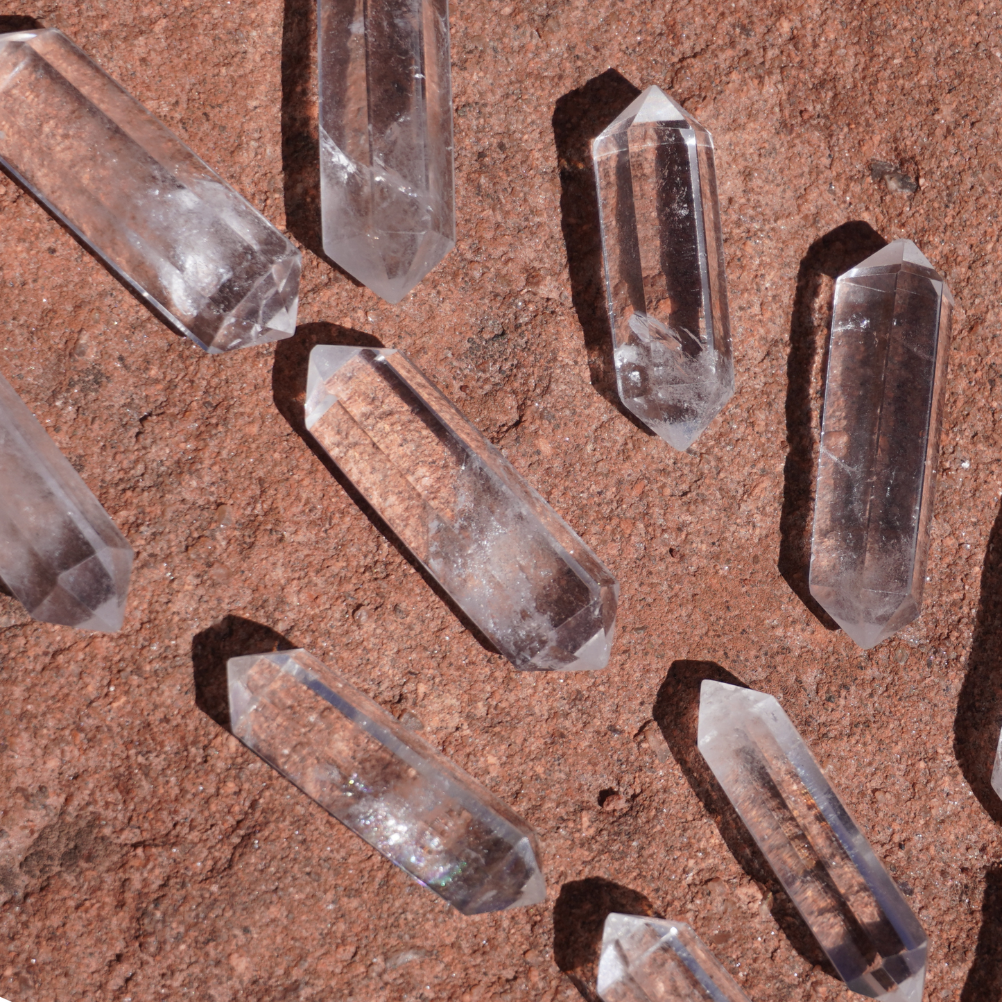 Multiple double terminated clear quartz crystals on red rock, used for energy alignment and intention setting.