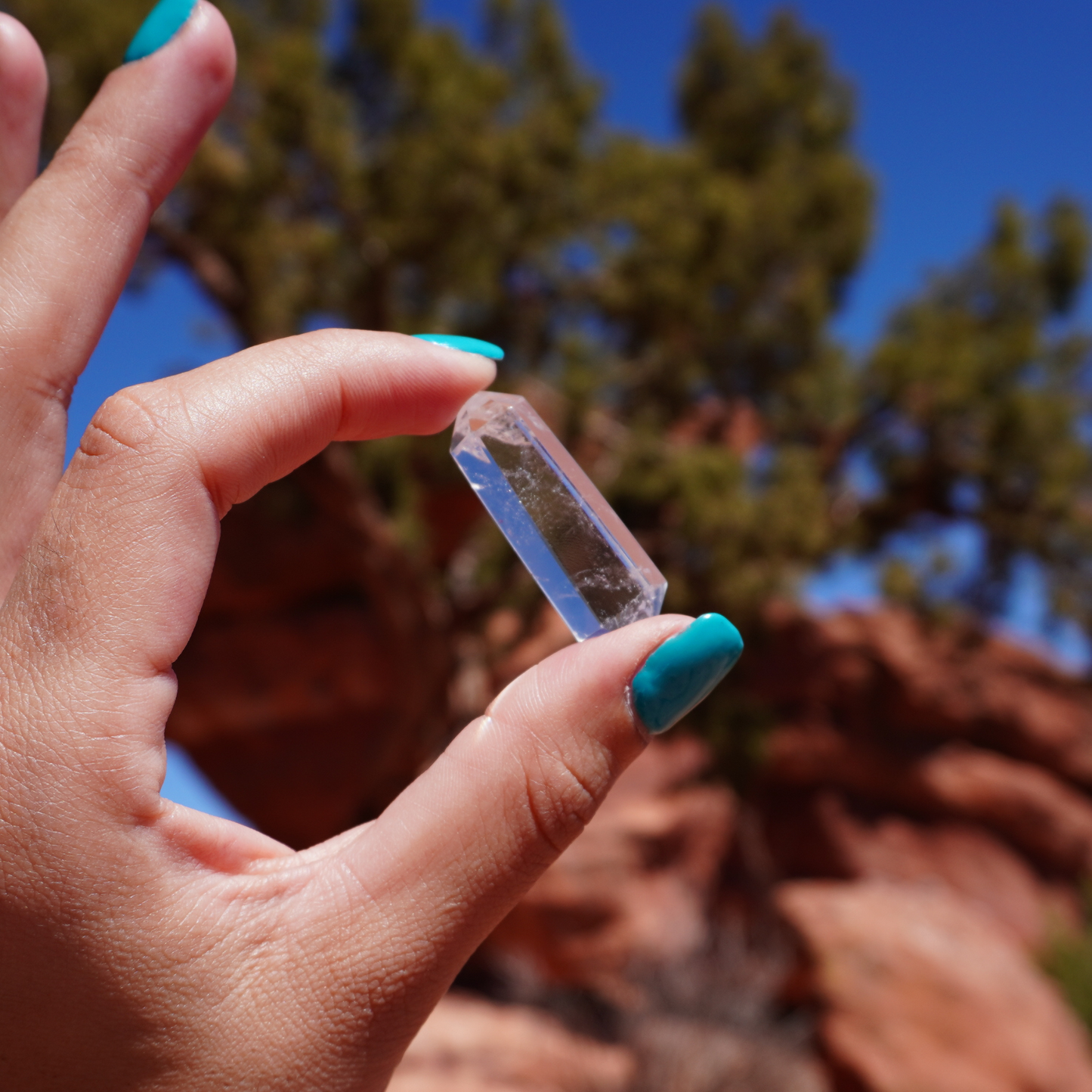Double terminated quartz crystal held in sunlight with trees in background, symbolizing amplified energy