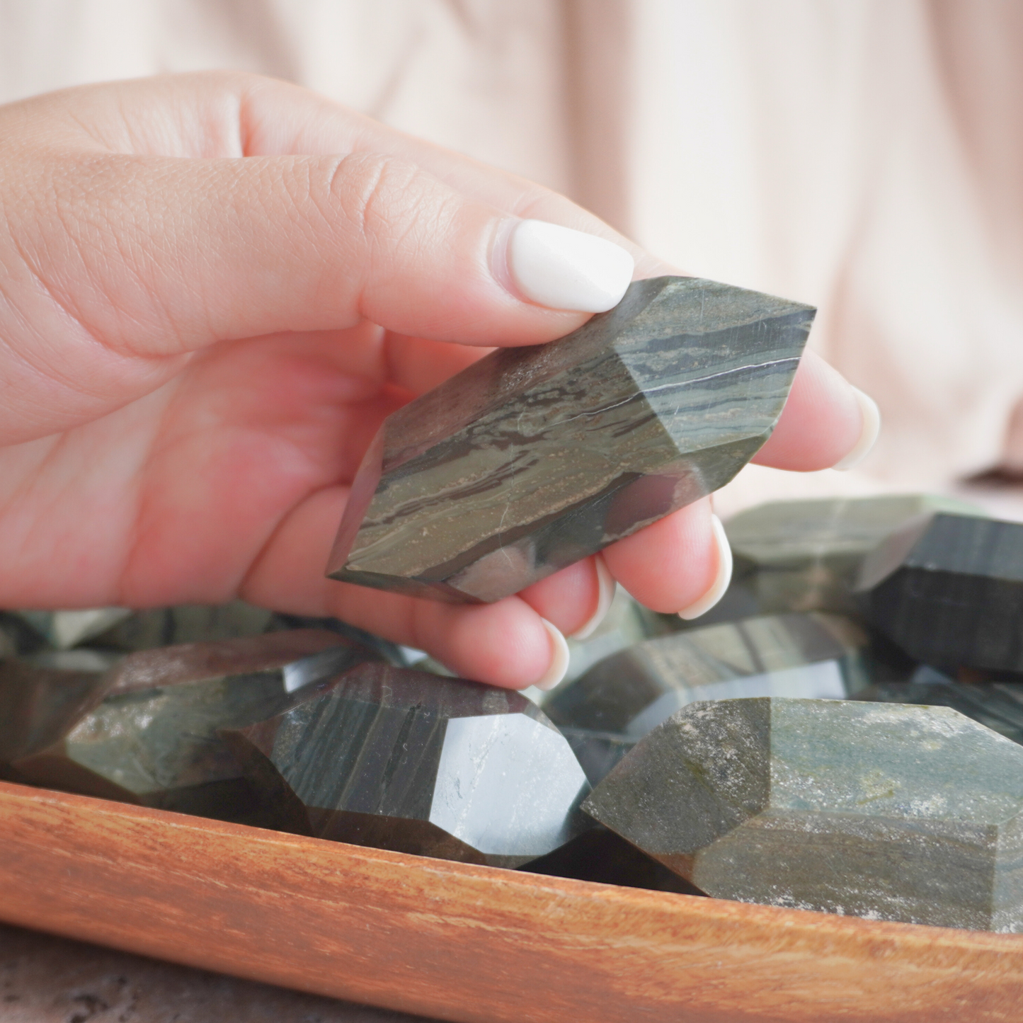 A hand holding a Green Zebra Jasper crystal point, perfect for meditation and stress relief.