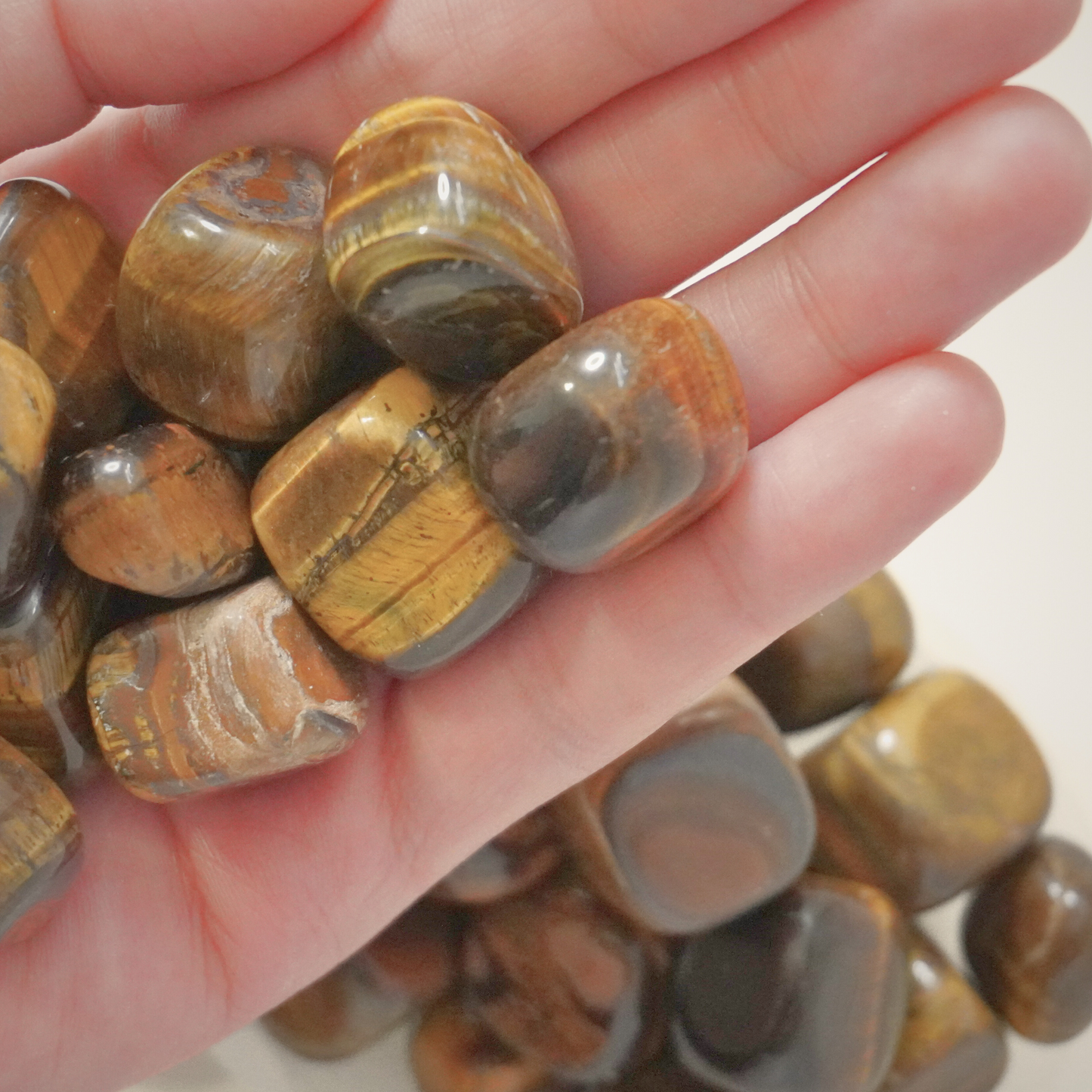 A hand holding a group of polished Tiger's Eye tumbles, showcasing their golden-brown shine and smooth finish.