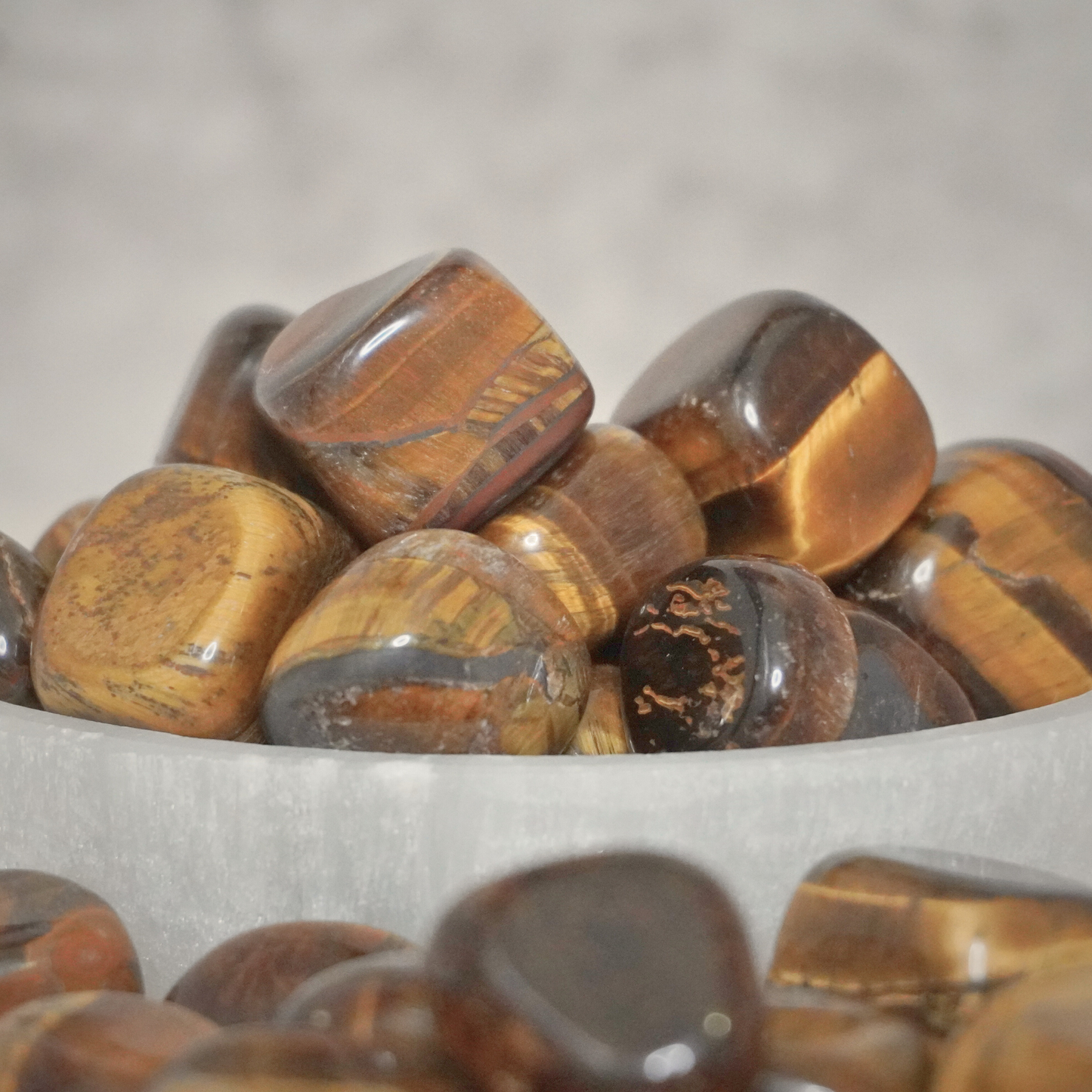 A bowl filled with polished Tiger's Eye tumbles, emphasizing their grounding, protective energy, and vibrant brown-gold color.