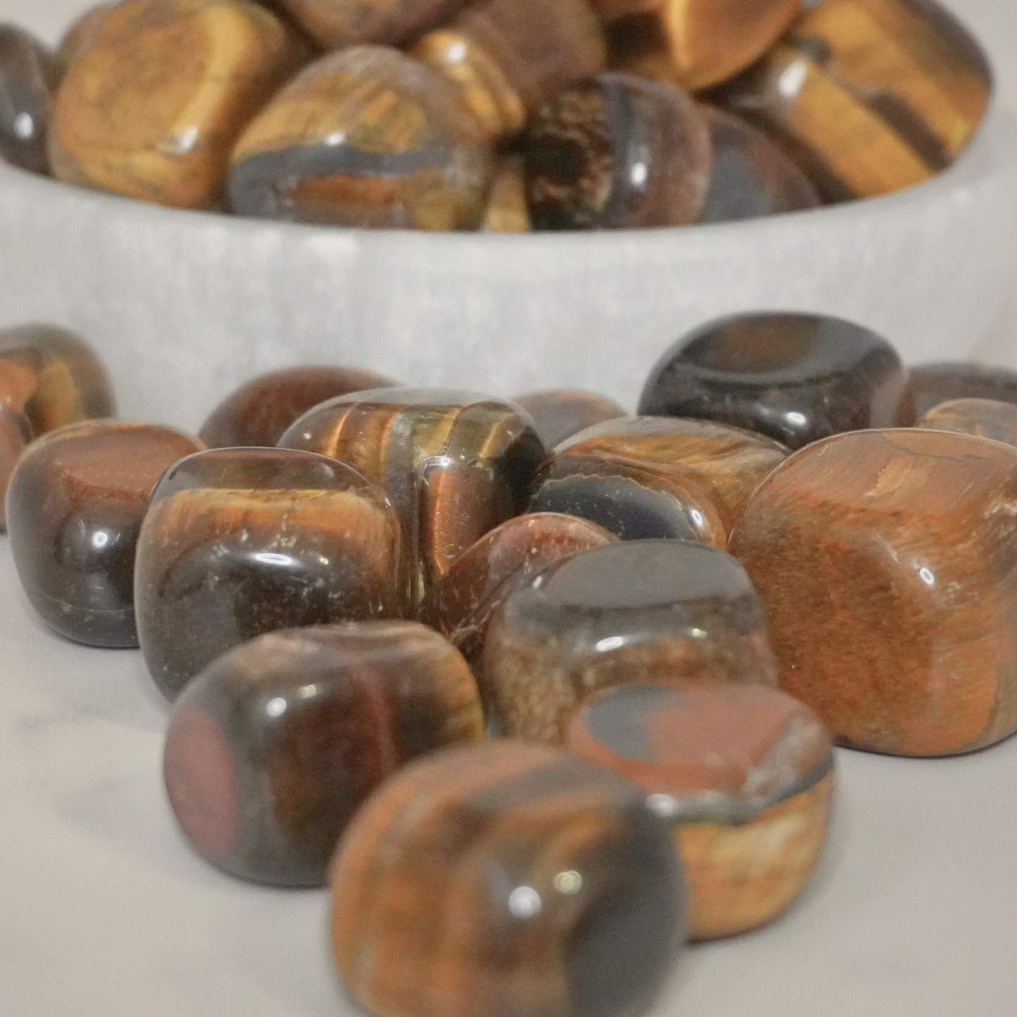 A close-up of polished Tiger's Eye tumbles scattered on a table, highlighting their protective and grounding qualities.