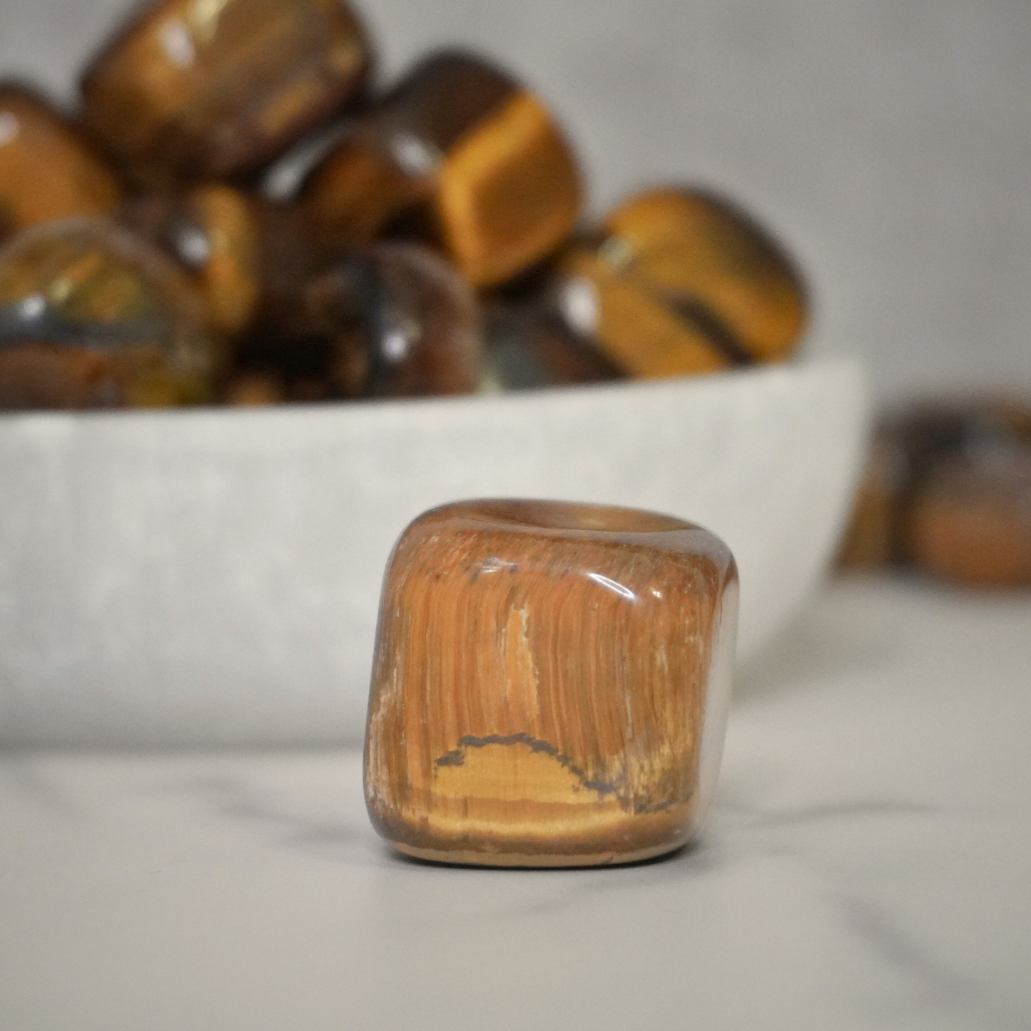 A single Tiger's Eye tumble standing upright with others in the background, showcasing the stone's earthy tones and grounding energy.