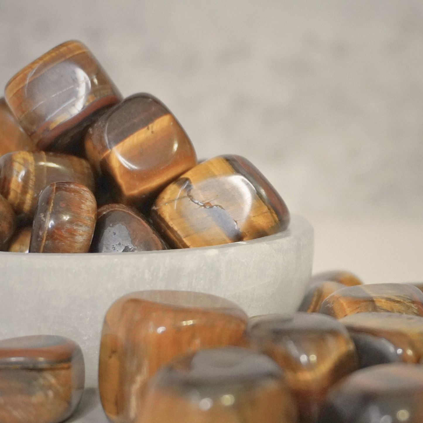 A bowl filled with polished Tiger's Eye tumbles, emphasizing their grounding, protective energy, and vibrant brown-gold hues.