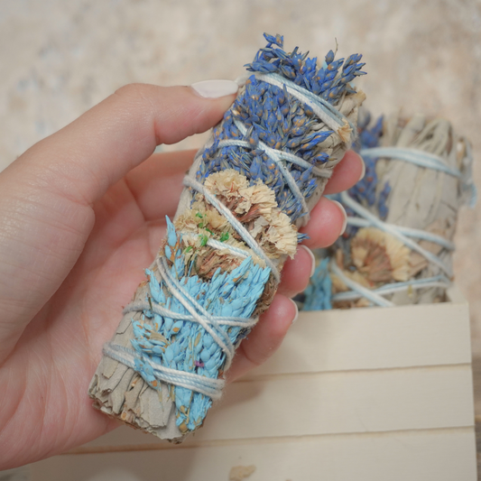 A hand holding a California white sage and sinuata flower bundle, showcasing its natural beauty for meditation and sacred rituals.