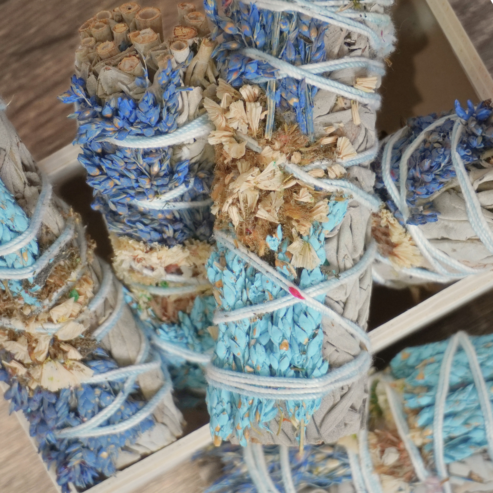 Top-down view of California white sage smudge bundles with colorful sinuata flowers, packed in a rustic wooden box for rituals.